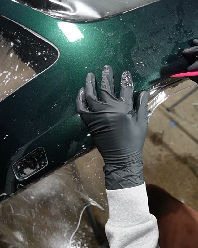 Paint protection film being squeegeed onto a green bumper
